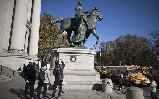 Visitors to the American Museum of Natural History in New York City look at a statue of Theodore Roosevelt, flanked by a Native American man and African American man, on November 17, 2017. The statue will be coming down after the museum's proposal to remove it was approved by the city (AP Photo/ Mary Altaffer/ File)