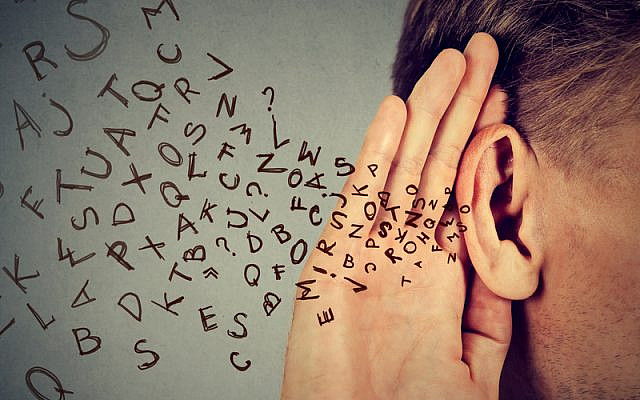 man holds his hand near ear and listens carefully alphabet letters flying in isolated on gray wall background