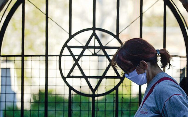 A masked woman passes by the Star of David outside a shul. Jewish communities have been disproportionately affected by the virus. (Photo by Artur Widak/NurPhoto via Jewish News)