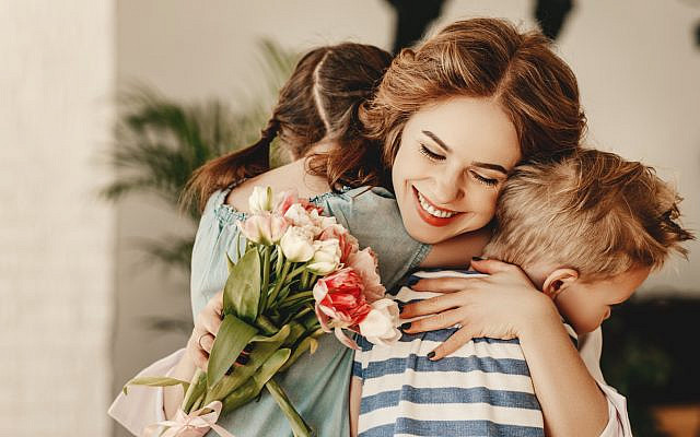 A smiling mother hugs her son and daughter, holding flowers they've given her. (iStock)