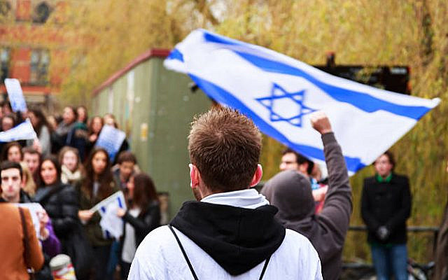 Birmingham, United Kingdom - November 28, 2012: Man wearing white t-shirt over a black hoody, shot from behind, watching a pro-Israeli demonstration in progress. In front of him a man holding up a clenched fist, and an unseen man in the crowd waving a large Israeli flag. The crowd is out of focus due to depth of filed and the main focus being on the observer rather than the crowd.