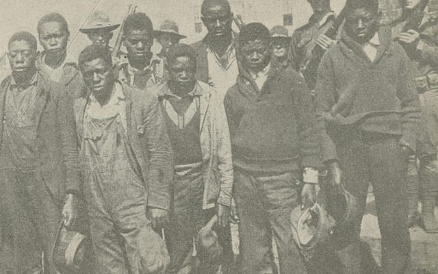 Black ink on yellowed paper. At center, a photograph of men marching in support of the Scottsboro boys.