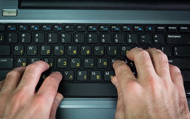 A man types on a computer keyboard with Hebrew and English letters. (iStock)