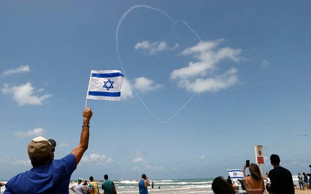 An Israeli man waves a flag as Israeli Efroni T-6 Texan II planes perform stunts in the sky above the Mediterranean coastal city of Tel Aviv on May 5, 2022, as Israel marks Independence Day (Yom HaAtzmaut), 74 years since the establishment of the Jewish state. - Israel's first prime minister David Ben-Gurion declared the existence of the State of Israel in Tel Aviv in 1948, ending the British mandate. (Photo by JACK GUEZ / AFP) (Photo by JACK GUEZ/AFP via Getty Images) An Israeli man waves a flag as Israeli Efroni T-6 Texan II planes perform stunts in the sky above the Mediterranean coastal city of Tel Aviv on May 5, 2022, as Israel marks Independence Day (Yom HaAtzmaut), 74 years since the establishment of the Jewish state. - Israel's first prime minister David Ben-Gurion declared the existence of the State of Israel in Tel Aviv in 1948, ending the British mandate. (Photo by JACK GUEZ / AFP) (Photo by JACK GUEZ/AFP via Getty Images)