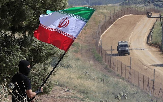 A Hezbollah supporter marking 'Liberation Day,' the 23rd anniversary of Israel's withdrawal from southern Lebanon in May 25, 2000, waves an Iranian flag in front of a passing Israeli armored vehicle, on the Lebanese-Israeli border in the southern village of Kfar Kila, May 25, 2023. (AP Photo/Mohammed Zaatari)