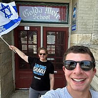 Tali and Andrew outside Golda Meir School entrance with Israeli Flag from pro-democracy protest movement.
