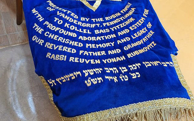 The cover of the Torah was designed when it was donated to a synagogue in Pittsburgh. It  reads:
Presented by the Rubin Family of Vandergrift, Pennsylvania to Kollel Bais Yitzchok with profound adoration and esteem for the cherished memory and legacy of pir revered father and grandfather Rabbi Reuven Yonah Rubinovitz