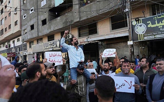 Palestinians in Deir al-Balah, in the central Gaza Strip, hold anti-war signs as a man chants slogans in support of the people of Beit Lahiya, in northern Gaza, who have been protesting against Hamas, March 26, 2025. (AP/Abdel Kareem Hana)