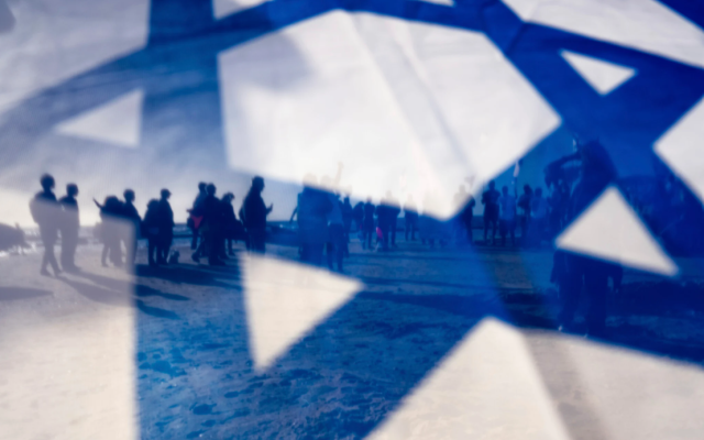 Israeli demonstrators are seen through Israel's national flag during a protest against plans by Prime Minister Benjamin Netanyahu's government to overhaul the judicial system, in Caesarea, Israel, March 17, 2023. (AP Photo/Oded Balilty)