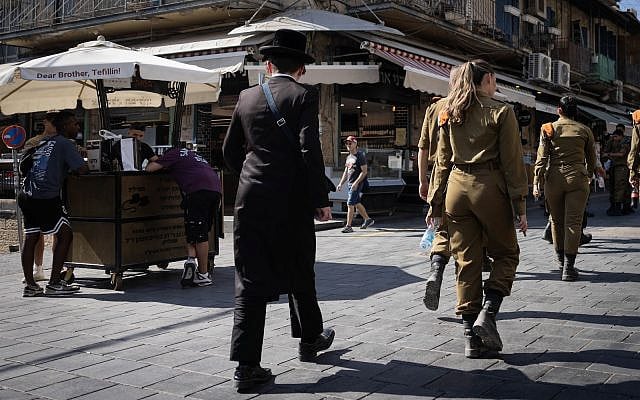 An Ultra orthodox Jewish man walks next to a female soldier at the Mahane Yehuda Market in central Jerusalem on August 27, 2023. (Chaim Goldberg/Flash90) An Ultra orthodox Jewish man walks next to a female soldier at the Mahane Yehuda Market in central Jerusalem on August 27, 2023. (Chaim Goldberg/Flash90)