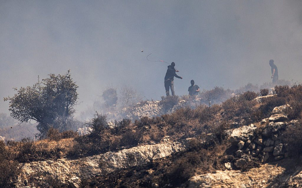 Masked settlers hurl rocks at Palestinians from the top of a hill in the West Bank village of Sinjil, July 4, 2025. (JOHN WESSELS / AFP)