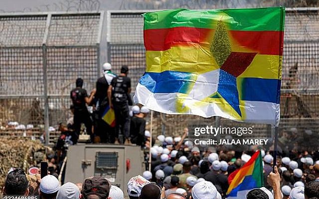 TOPSHOT - Members of the Druze community demonstrate before Israeli forces by the barbed-wire fence separating the Israeli-annexed Golan Heights and Syria near Majdal Shams on July 16, 2025. Israeli troops on July 16 sought to control crowds and prevent Druze from crossing the border with Syria, after deadly violence in the country's south that prompted Damascus to send in government forces. (Photo by Jalaa MAREY / AFP) (Photo by JALAA MAREY/AFP via Getty Images)