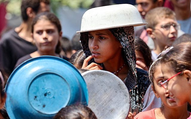 A displaced Palestinian girl covers her head with a pot to protect herself from the scorching sun as she waits at a food distribution point in Gaza City in the northern Gaza Strip on July 25, 2025. (Omar AL-QATTAA / AFP)