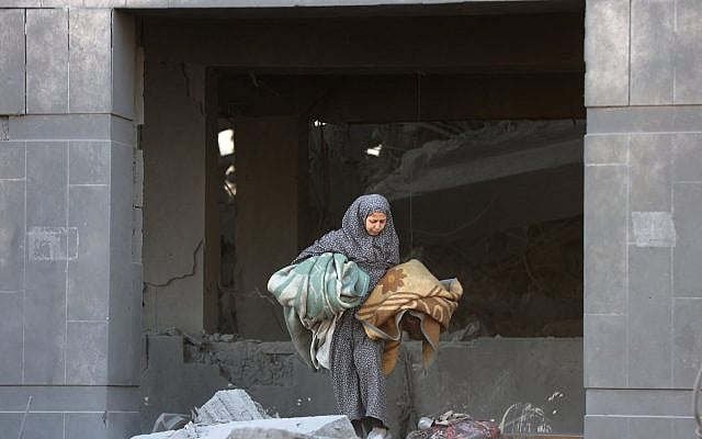 Illustrative. A Palestinian woman carries her belongings as she walk on debris after an overnight strike on the Sheikh Radwan Health Centre run by the United Nations Relief and Works Agency for Palestine Refugees (UNRWA) in the north of Gaza City on August 6, 2025. (Omar al-Qattaa/AFP)