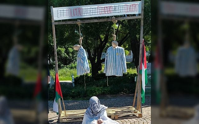 A display in Umeå Sweden shows two effigies in Holocaust uniforms hanging from nooses under a banner reading 'A genocide is a genocide.' Below is a mannequin dressed in Palestinian attire, flanked by Palestinian flags. August, 2025 (Courtesy)