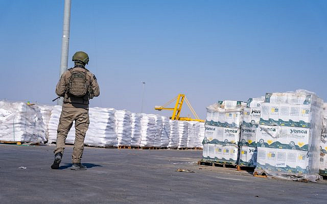 A soldier stands near aid packages on the Gazan side of the Kerem Shalom Crossing, in the southern Gaza Strip, July 24, 2025. (Emanuel Fabian/Times of Israel)