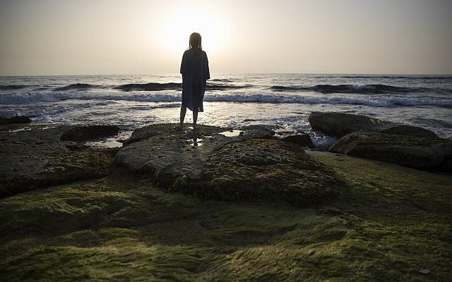 ILLUSTRATIVE: A young Israeli is silhouetted during sunset at the beach in the northern city of Naharia on April 28, 2017. (Nati Shohat/Flash90)