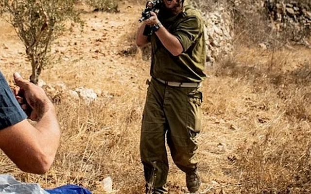 A settler wearing a soldier's uniform aims his gun at Jews and Palestinians participating in an olive harvest in the West Bank, Nov. 4, 2025. (Courtesy Sarah Reines)