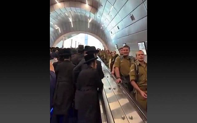 Haredi men ascend, and IDF soldiers descend, the escalators at the Yitzhak Navon train station in Jerusalem, ahead of a mass Haredi rally against conscription, on October 30, 2025. (Screen capture via Yehonatan Cohen)