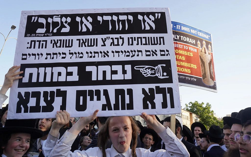 Haredi boy holds sign that reads: 'Our answer to the High court and the rest of the haters of religion: Even if you stand us in front of a firing squad, we will choose death, and not enlist to the army,' at a protest against the draft in Jerusalem on August 7, 2025. (Charlie Summers/Times of Israel)