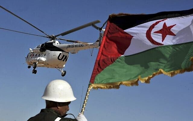A soldier holds the Algerian flag as a United Nations helicopter files over the Smara refugees camp near Tindouf, south-western Algeria, Saturday, March 5, 2016. Ban Ki-moon will meet with leaders of the Polisario Front, the organization disputing sovereignty over Western Sahara with Morocco, in the hope to help solving a 40-year conflict. (AP Photo/Toufik Doudou)