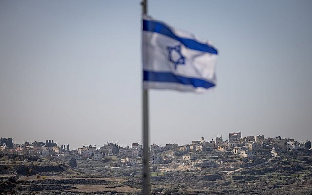 An Israeli flag in the Israeli settlement of Kedumim is seen in the foreground of a Palestinian village in the West Bank. January 7 2025. (Chaim Goldberg/Flash90)