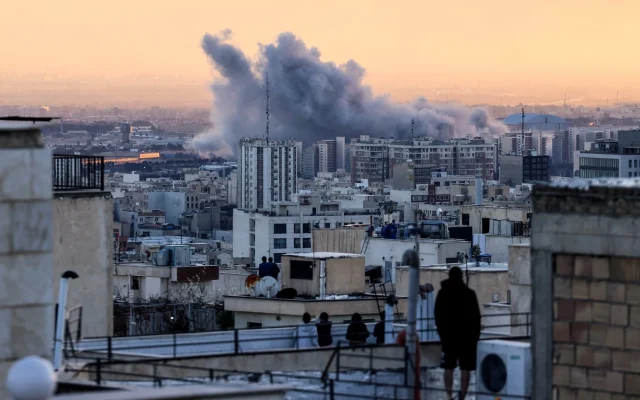 A person stands on the roof of a building looking at a plume of smoke rises after a strike on the Iranian capital Tehran, on March 3, 2026. (Photo by ATTA KENARE / AFP)