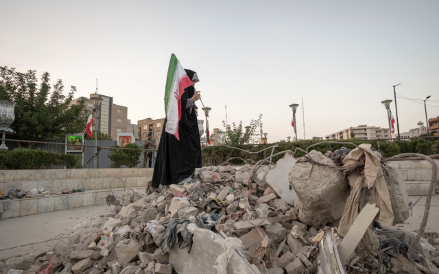 A veiled Iranian art student holds a country flag while standing on symbolic debris of a destroyed building as she performs in an anti-war conceptual play at a square in downtown Tehran, Iran, on Saturday. Photograph: NurPhoto/Getty Image