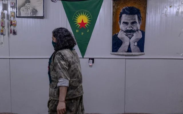 A female Kurdish fighter from the Iranian Kurdish armed faction Kurdistan Free Life Party (PJAK) passes a poster of Abdullah Ocalan, the jailed founder of the Kurdistan Workers' Party (PKK), at a site near the Iraqi border with Iran in Iraq's autonomous Kurdistan region, on March 8, 2026. (Photo by AFP)