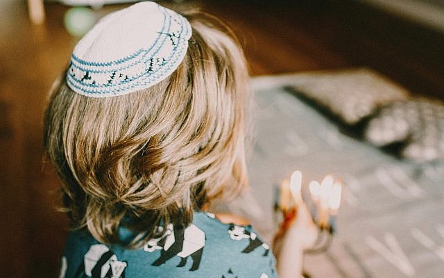 A child wearing a kippah lights Shabbat candles. | Photo: Pexels