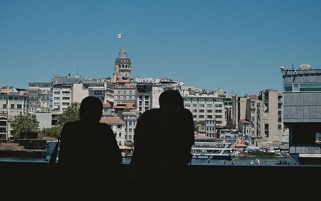 Two silhouettes view the Galata Tower and skyline from across the water on a sunny day in İstanbul, free download available for non-commercial and commercial use as downloaded from the website Pexels (https://www.pexels.com/photo/silhouettes-overlooking-galata-tower-in-istanbul-38298154/).