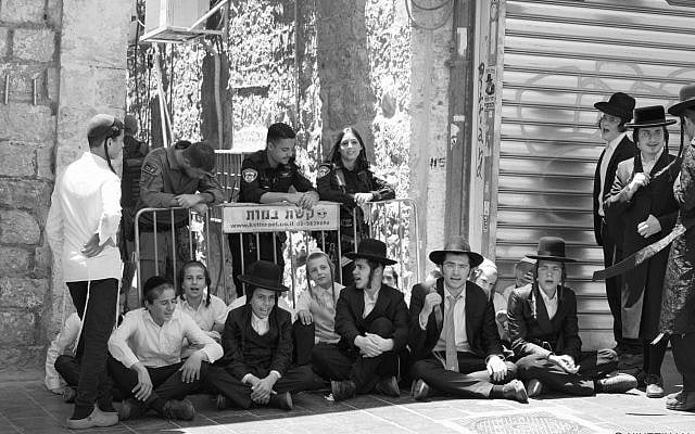 Overseen by police, young Haredim sit in an alley outside Cafe Basimta, Shabbat morning, in protest of the cafe being open, August 8, 2026. (courtesy of my wife)