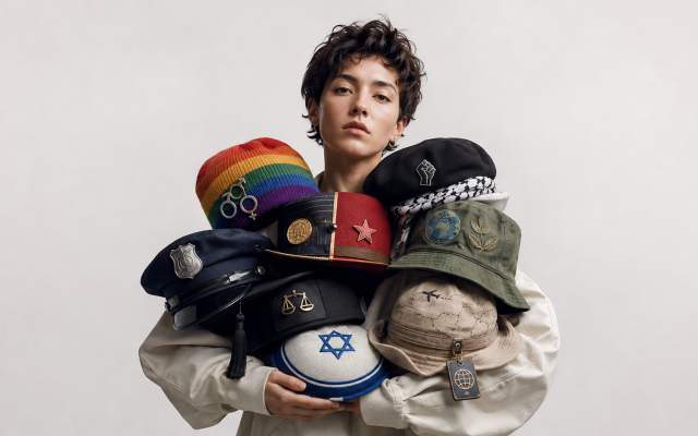 A young activist holds a collection of symbolic hats representing gender politics, socialism and capitalism, racial activism, climate change, policing, immigration, Israel, and other modern political causes. The image illustrates how separate social issues are increasingly packaged together into broader ideological identities.