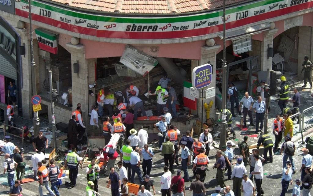 Police and medics surround the scene of a suicide bombing inside Jerusalem's Sbarro restaurant, August 9, 2001. Fifteen people were killed, and 130 injured. A 16th victim died in 2023. (AP/Peter Dejong)