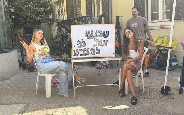 Two aspiring journalists from Israel Hayom, both in their mid-twenties, sitting at a stand at the Nachalat Binyamin art fair in Tel Aviv. Their sign reads: "Convince me who to vote for."