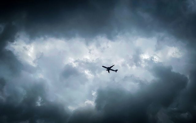 An aircraft flies beneath storm clouds, symbolising courage and hope in moments of crisis. Photo: Chongdong Zhu / Unsplash.