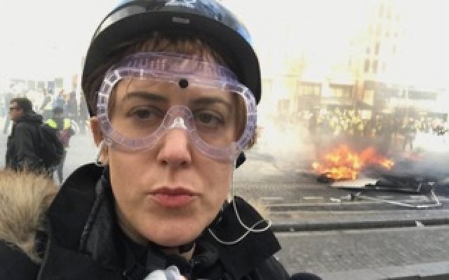Paula Slier reporting during the Yellow Vest protests in Paris, 2018-2019, as a fire burns in the street behind her. (Photo: Personal archive)