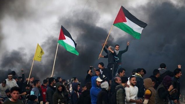 توضیح تصویر: تزئینی، معترضین فلسطینی با پرچم ملی حین زدوخورد با مأموران امنیتی اسرائیلی در حومه‌ی شرقی شهر غزه، نزدیک مرز اسرائیل، ۱۲ ژانویه ۲۰۱۸. (AFP Photo/Mohammed Abed)