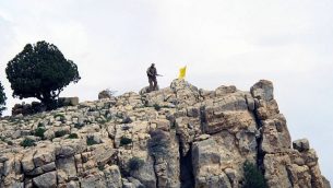 توضیح تصویر: در عکسی از شنبه ۹ مه ۲۰۱۵، یک رزمنده‌ی حزب‌الله در کنار پرچم گروه بر تپه‌ای در دشت‌های مجاور شهر اصال الورد در ناحیه‌ی کوهستانی قلمون، سوریه ایستاده است. (AP Photo/Bassem Mroue, File)