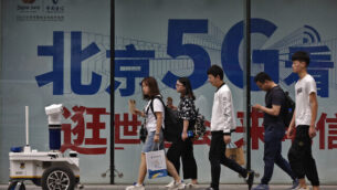 People walk toward a police robot mounted with surveillance cameras patrol past a 5G network advertisement at a shopping district in Beijing, Wednesday, May 15, 2019. U.S. officials listed $300 billion more of Chinese goods for possible tariff hikes while Beijing vowed Tuesday to "fight to the finish" in an escalating trade battle that is fueling fears about damage to global economic growth. (AP Photo/Andy Wong)