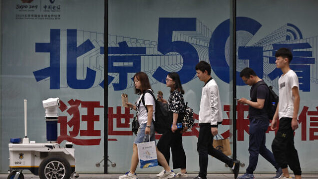 People walk toward a police robot mounted with surveillance cameras patrol past a 5G network advertisement at a shopping district in Beijing, Wednesday, May 15, 2019. U.S. officials listed $300 billion more of Chinese goods for possible tariff hikes while Beijing vowed Tuesday to "fight to the finish" in an escalating trade battle that is fueling fears about damage to global economic growth. (AP Photo/Andy Wong)