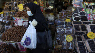 A woman wearing a protective face mask and gloves to help prevent the spread of the coronavirus carries her purchases as she leaves a store which sells dates, a favorite fruit for the Muslim holy fasting month of Ramadan, in southern Tehran, Iran, Monday, April 27, 2020. In Iran, the country that is hit worst in the Middle East by the coronavirus, all religious gathering, congregational prayers and communal Iftar servings, a meal eaten at sunset to break the fast, remain forbidden in the Ramadan and also holy shrines and religious centers also continue to be closed until at least May 4. (AP Photo/Vahid Salemi)