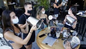 Mask-clad Israeli restaurant owners and clients protest against new lockdown measures imposed by the authorities due to a surge in coronavirus cases,  by banging ice buckets, in the Israeli coastal city of Tel Aviv, on July 17, 2020. - Israel's government said today it was imposing new restrictions to limit the spiralling spread of coronavirus in the hope of avoiding a general lockdown further along the line. (Photo by JACK GUEZ / AFP)