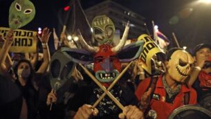 A protester wearing a horned-demon papier-mâché mask stands holding crossed drum sticks while flanked by another protester wearing a mask in the shape of a skull and signs showing alien heads raised behind, during a demonstration against the Israeli government near the Prime Minister's residence in Jerusalem on August 8, 2020. (Photo by Ahmad GHARABLI / AFP)