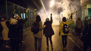 FILE - In this Jan. 11, 2020, file photo, protesters hold flowers as tear gas fired by police rises at a demonstration in front of Amir Kabir University in Tehran, Iran, to remember victims of a Ukrainian airplane shot down by an Iranian missile. The downing of a Ukrainian jetliner near Tehran on Jan. 8 highlights the limits of the civilian arm of Iran's government against the absolute power of the Shiite theocracy and the paramilitary forces beneath it. (AP Photo/File)
