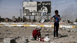 توضیح تصویر: در عکس ۱۲ مارس ۲۰۱۷ کودکان عراقی در میانه‌ی خرابه‌های خیابانی در محله‌ی نبولوس موصل در مقابل بیلبوردی با لوگوی داعش نشسته‌اند و همزمان نیروهای امنیتی برای بازپس‌گیری بخش‌های غربی شهر از داعش، حمله کرده‌اند
