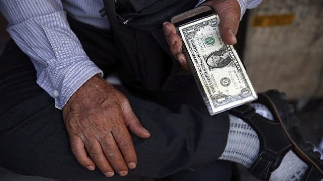 توضیح تصویر: یک فروشنده خیابانی ارز در ایران، در مرکز شهر تهران، اسکناس ایالات متحده را در دست دارد، تهران، ایران، 30 ژوئن 2018. (AP Photo/Vahid Salemi)