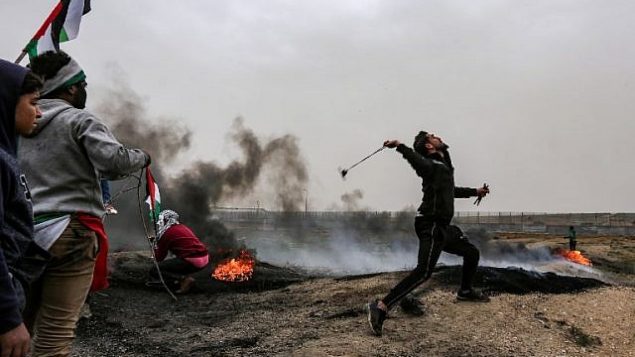 تصویر: یک معترض فلسطینی در زدوخوردهایی که در پی تظاهرات در امتداد مرز اسرائیل در ملاکه، شرق شهر غزه، با سنگ-قلاب به سمت نیروهای اسرائیل سنگ پرتاب می کند، ۳۰ مارس ۲۰۱۹. (Mahmud Hams/AFP)