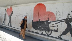 تصویر: مردی از اهالی افغانستان از کنار دیوارنگاره ای در نزدیکی محل بمباران مرگبار میگذرد که بر آن شعارهایی با مضمون «مرگ بر اسرائیل» نوشته شده. (Ezzatullah Mehrdad/ Times of Israel)