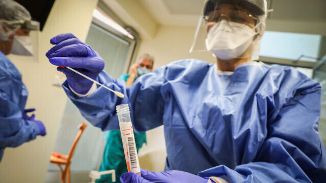 Hadassah Ein Kerem medical team members, wearing protective gear, are handling a Coronavirus test sample of Hadassah Ein Kerem workers at the Hadassah Ein Kerem Hospital in Jerusalem on March 24, 2020. Photo by Yossi Zamir/Flash90 *** Local Caption *** קורונה
וירוס
מגיפה
מגן דוד אדום
צוות רפואי
הצלה
בדיקות
נשאים
הדסה עין כרם